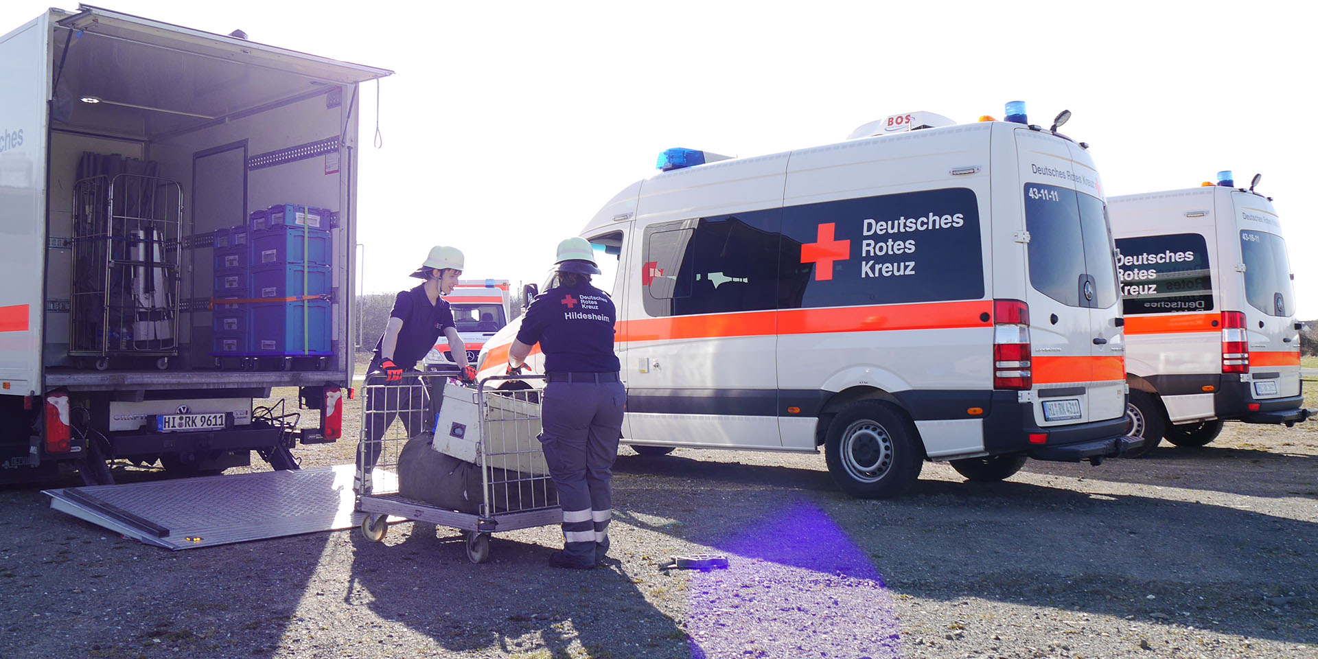 Einsatzkräfte laden Material aus einem LKW aus. Die Ladebordwand ist heruntergelassen. Rechts daneben stehen zwei MTWs.
