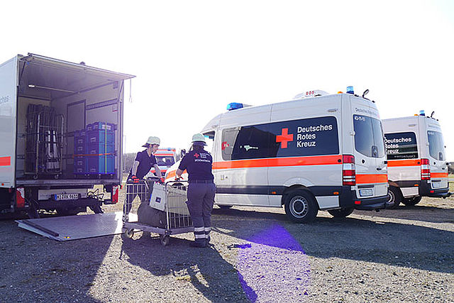 Einsatzkräfte laden Kisten aus LKW aus. Der LKW ist von hinten mit heruntergefahrener Ladebordwand zu sehen.