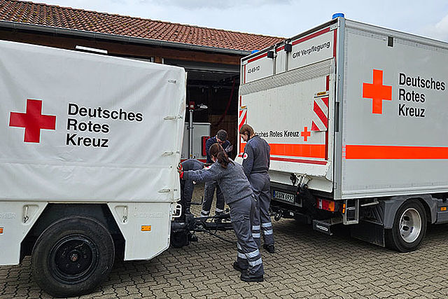 Einsatzkräfte hängen die DRK-Feldküche an den Gerätewagen Verpflegung an.