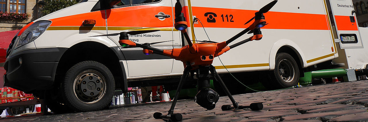 Drohne steht auf einer gepflasterten Fläche. Schräg von unten fotografiert.