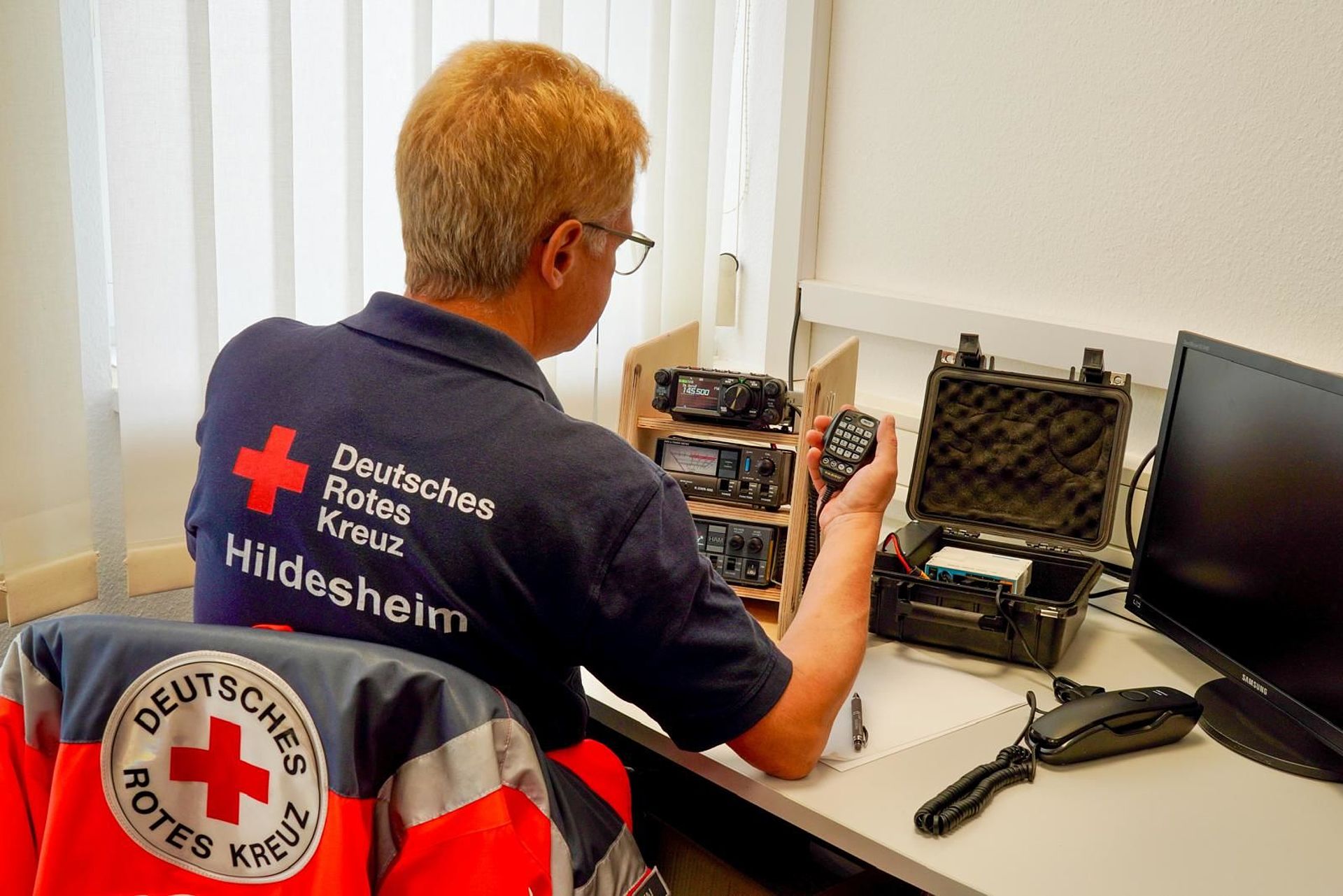 DRK-Einsatzkraft sitzt am Notfunk-Arbeitsplatz im ZfB. Von hinten fotografiert.