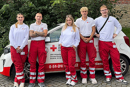 Junge Menschen in Einsatzkleidung vor einem DRK-PKW