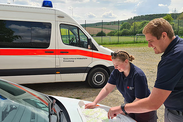 Nahaufnahme von zwei Einsatzkräften an der Motorhaube eines Fahrzeug. Beide sind nach vorn gebeugt und arbeiten an einer Karte.