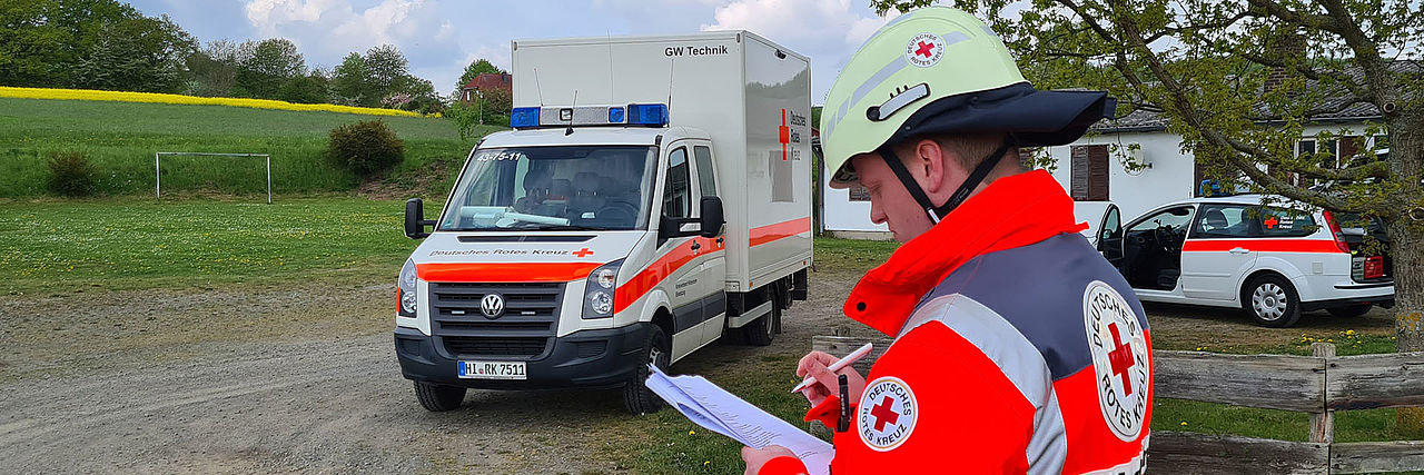 DRK-Einsatzkraft mit Klemmbrett vor LKW.