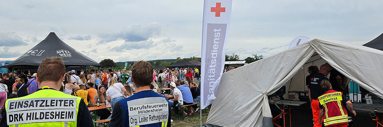 Sanitätsdienst bei Veranstaltung auf dem Volksfestplatz in Hildesheim. Im Vordergrund sind Einsatzkräfte von hinten mit Rückenschildern zu sehen: Einsatzleiter DRK Hildesheim, Organisatorischer Leiter Rettungsdienst.