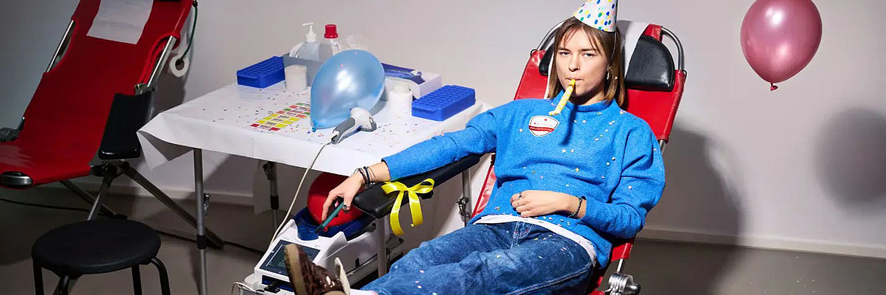 18jähriger liegt auf einer Blutspende-Liege, umgeben von Party-Utensilien wie Luftballons.