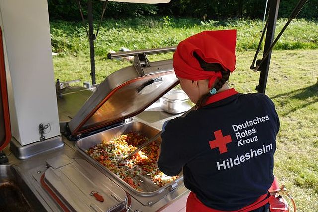 Einsatzkraft kocht in der Feldküche mit geöffnetem Kessel.