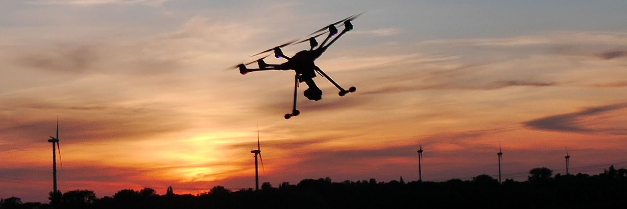 Drohne vor Sonnenuntergang mit Bäumen und Windrad.