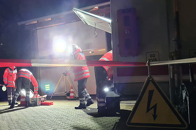 Einsatzszenario im Dunklen, ein Teil des Fotos ist ausgeleuchtet, Einsatzkräfte bauen Stromversorgung auf.