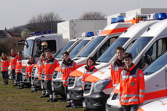 Gruppenfoto Einsatzkräfte und Fahrzeuge schräg von vor fotografiert.