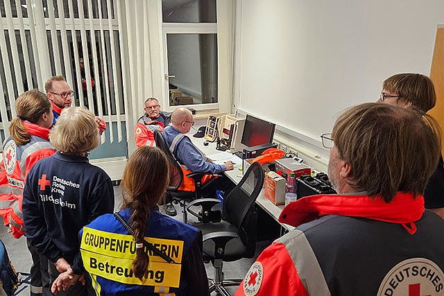 Mehrere Einsatzkräfte, die von hinten zu sehen sind, besichtigen eine Funkstation.