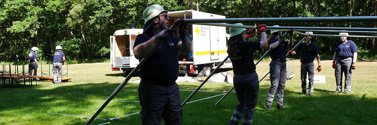 Einsatzkräfte bauen ein Zelt auf einer Rasenfläche auf.