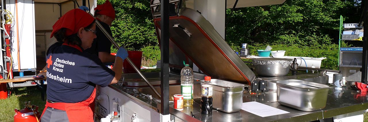 Eine Einsatzkraft bereitet Essen in der Feldküche vor. Der Kessel ist geöffnet. Es dampft.